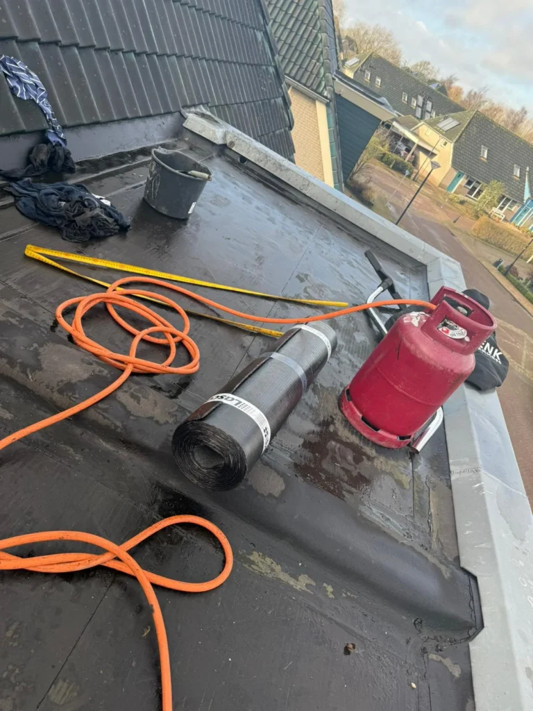 Dakrenovatie in Nijkerk met nieuwe bitumen dakbedekking en hergebruik van zinken dakranden op een dakkapel.